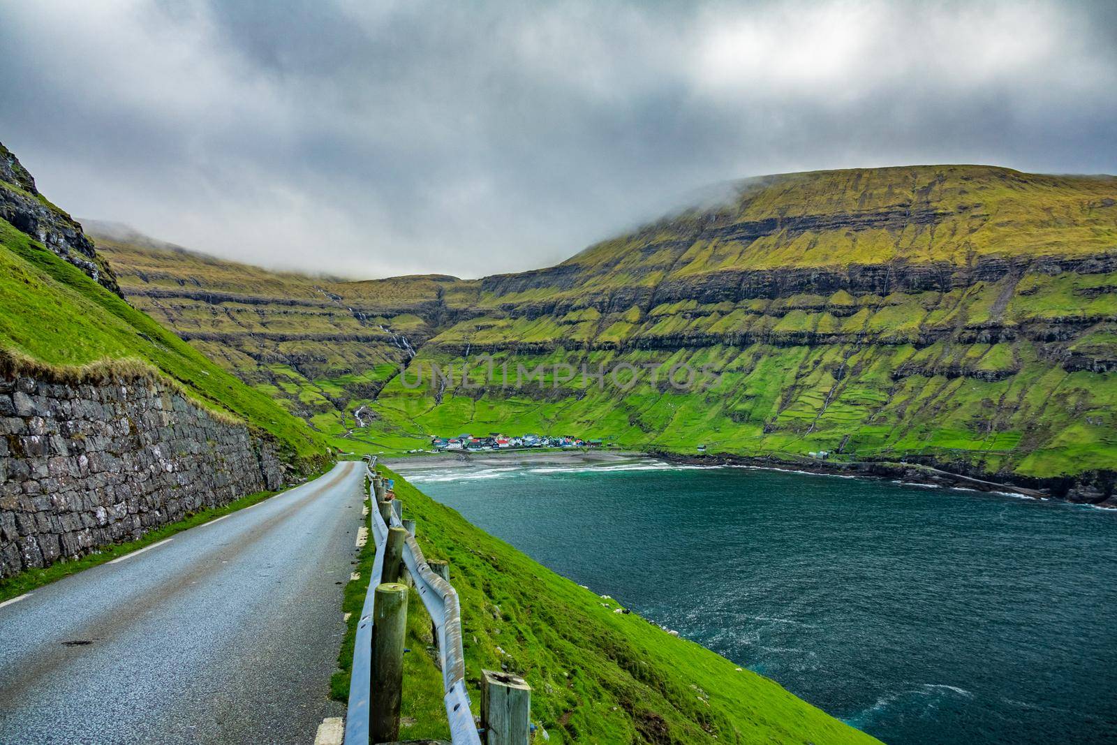 Road to Tjornuvik village surrounded by green mountains in bay, Faroe Islands