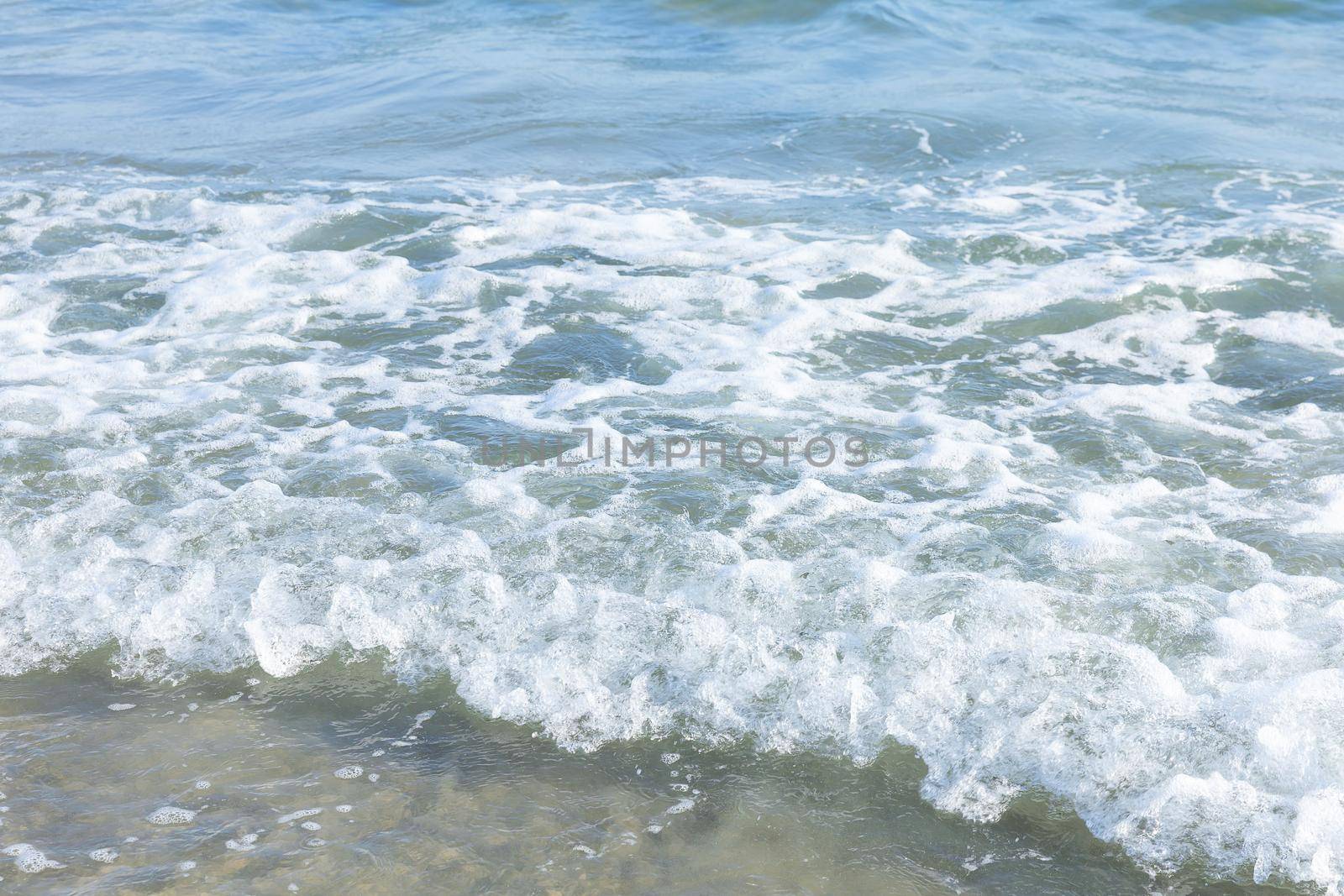 Sea water wave with foam on the beach in sunny day