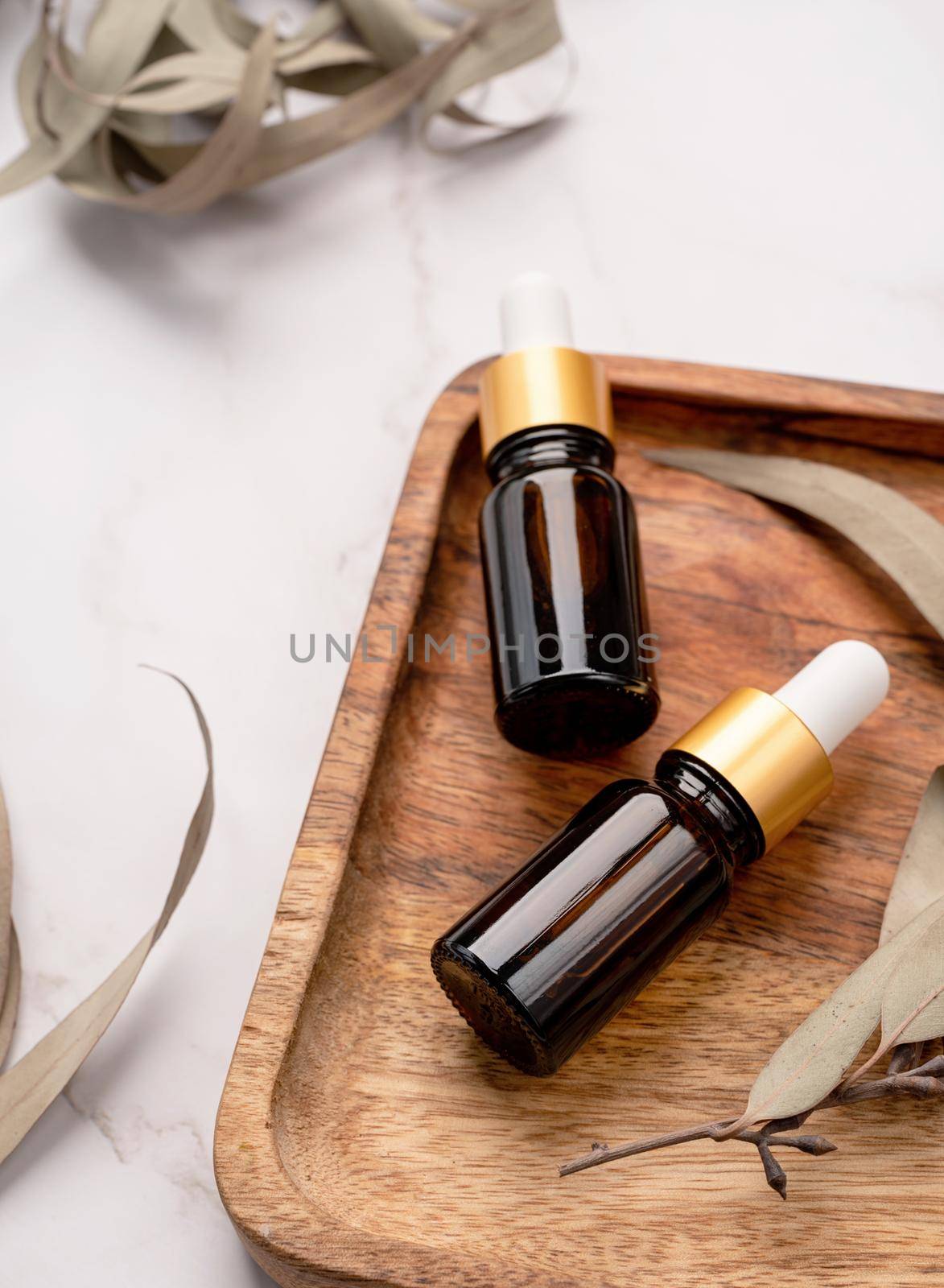 top view of Blank amber glass essential oil dropper bottle with pipette on concrete background with eucalyptus leaves, mock up design