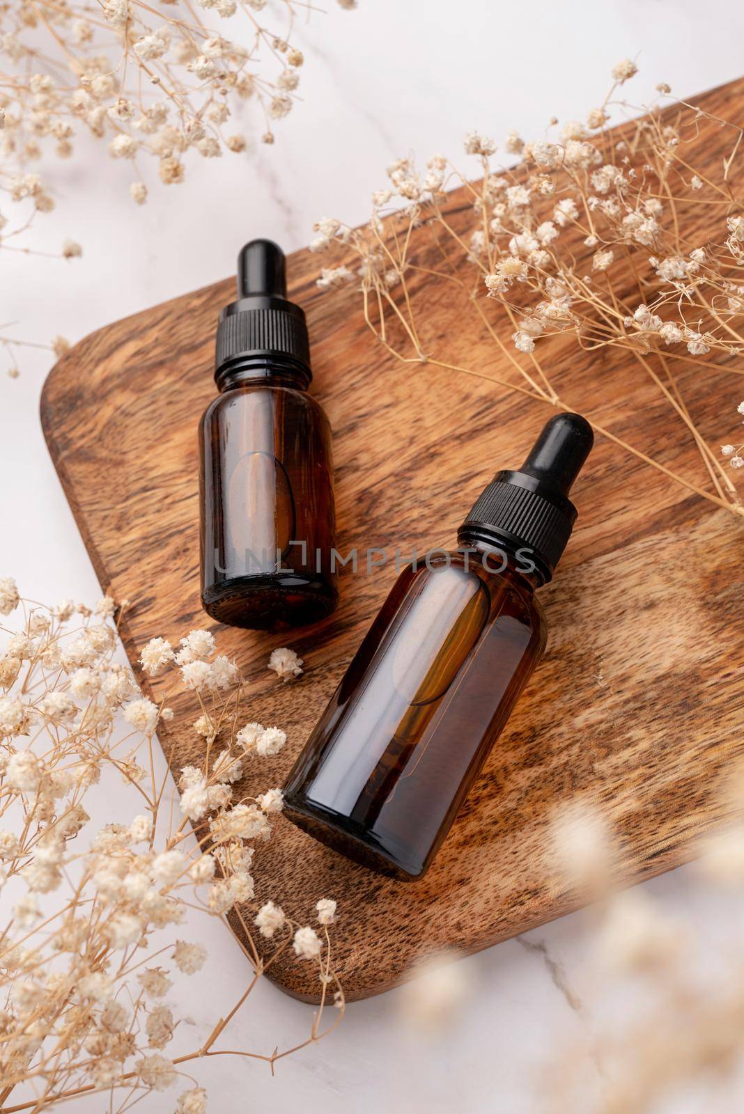 amber glass essential oil dropper bottle with pipette on concrete background with white flowers, mockup design