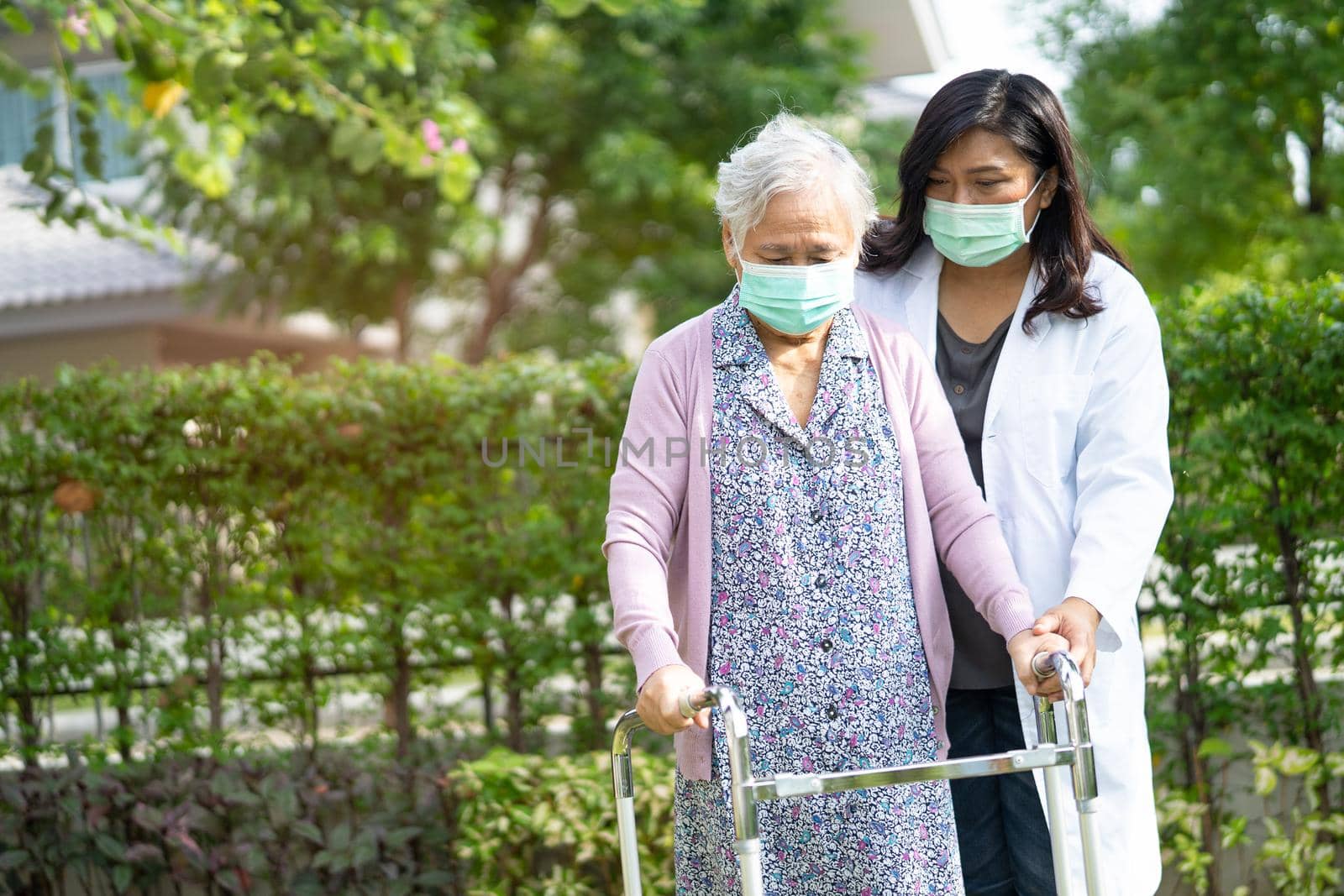 Doctor help Asian senior or elderly old lady woman walk with walker and wearing a face mask for protect safety infection and kill Novel Coronavirus Covid-19 virus.