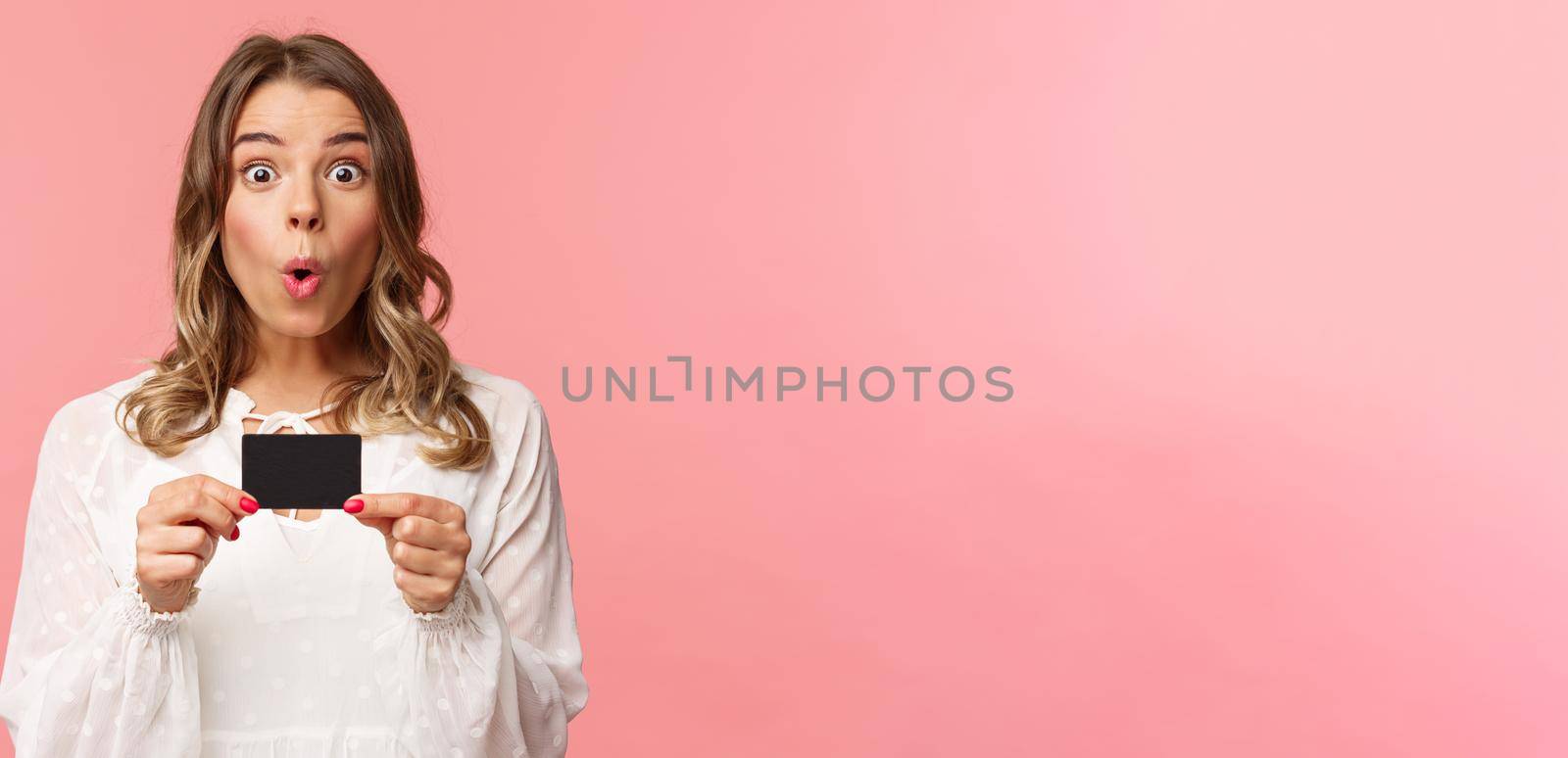Close-up portrait of excited and amused young girl describe new features of her bank, received new credit card, say wow, folding lips thrilled and amazed, standing pink background.