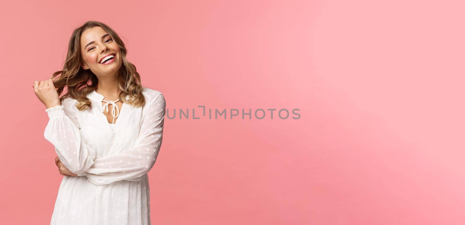 Waist-up portrait gorgeous blond woman with makeup and curly hairstyle, getting ready for going out on date, walk along park on fine spring day, smiling feeling happy, pink background.