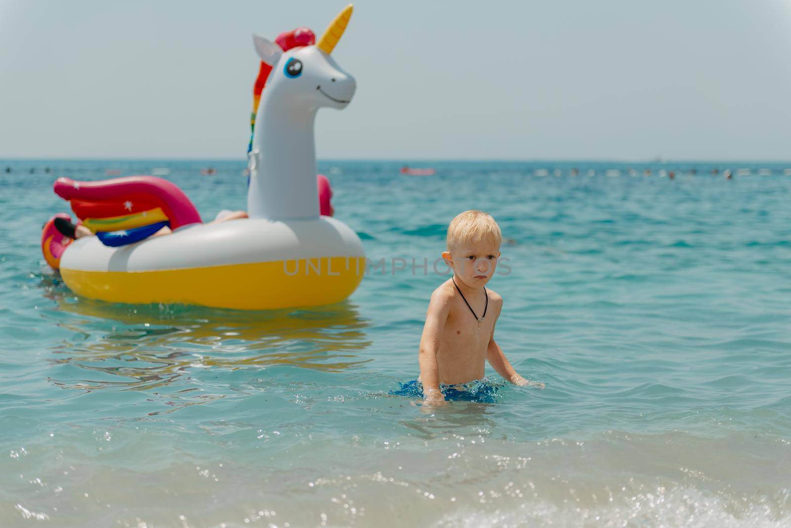 Child learning to swim in the open sea of tropical resort. Kids learn swimming. Exercise and training for young children. Little boy with colorful float board in sport club. Swimming baby or toddler. Happy child boy swims in sea in swimming circle with splash. Blue sky and water. Swimming training. Fun joy activities on vacation in the beach. Childhood moments lifestyle. Freedom careless. boy swim in the sea.