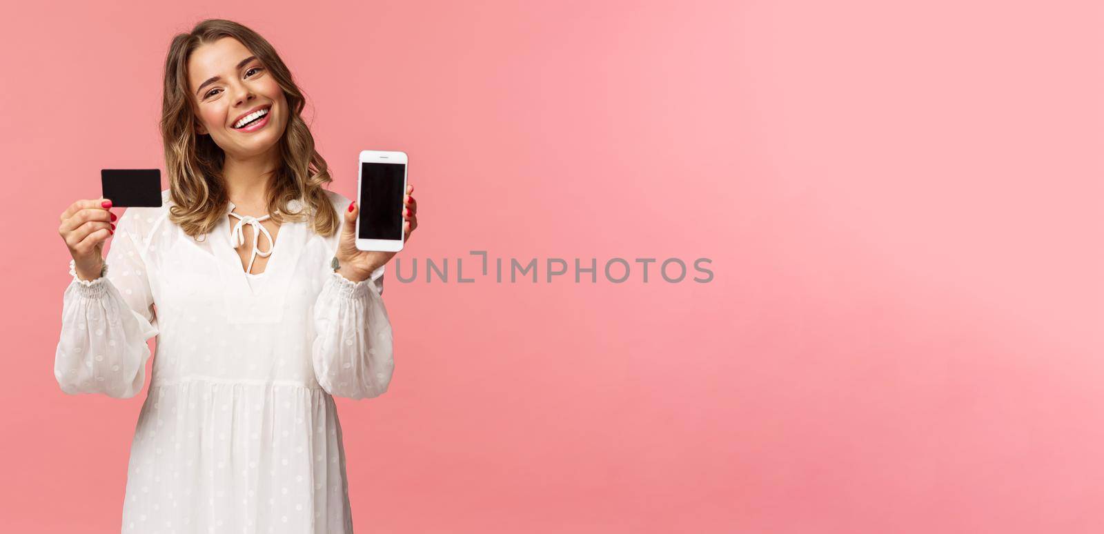 Portrait of tender feminine young blond girl in white dress, tilt head and smiling pleased, advice download application, holding mobile phone, credit card, show smartphone screen, pink background by Benzoix