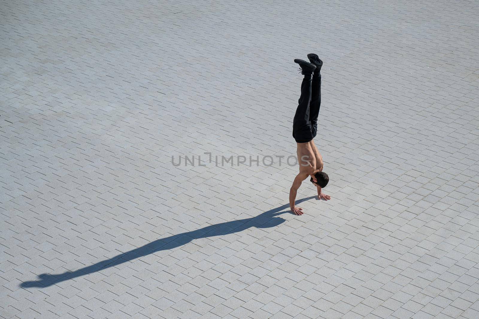 Shirtless man walks on his hands outdoors. View from above