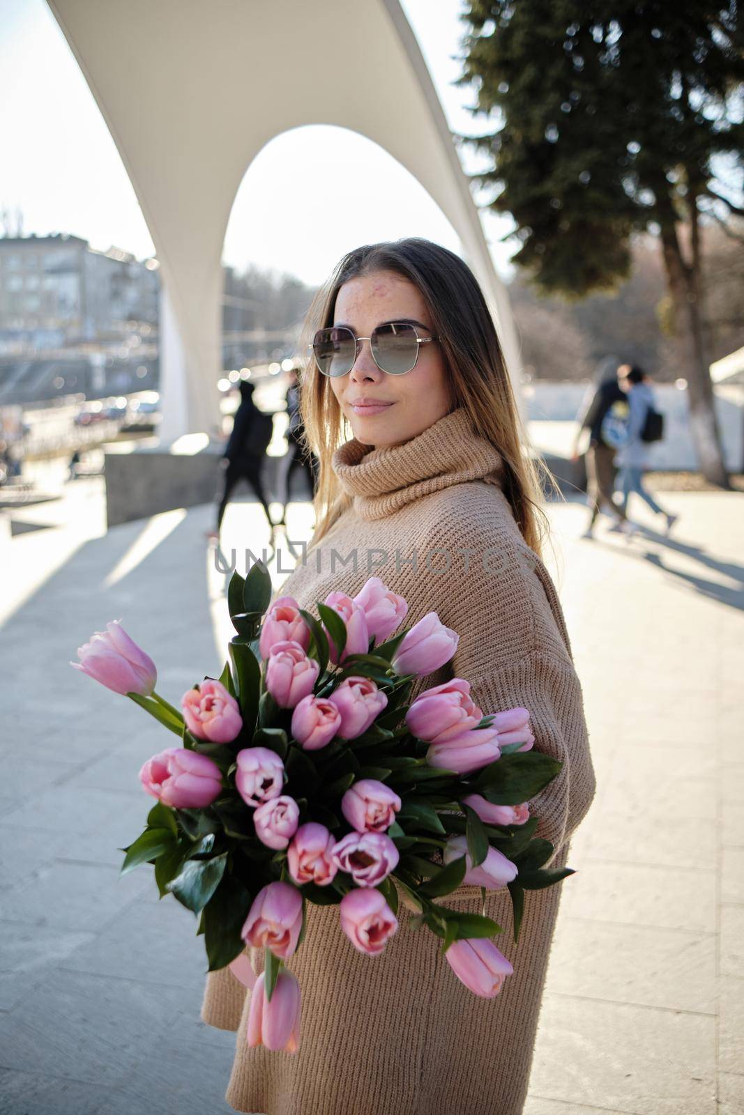 Young beautiful smiling hipster woman in trendy summer sundress. Sexy carefree woman posing on the street background in hat at sunset. Positive model outdoors on embankment. Holding flowers outdoors