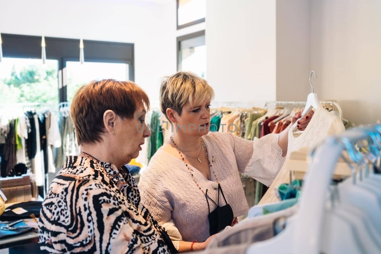 Mature shop assistant giving fashion advice to elderly customer. Shopping concept by CatPhotography