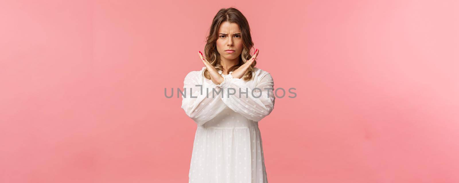 Portrait of serious-looking confident and displeased young blond woman make stop sign, cross arms over chest and frowning with disapproval, prohibit, reject bad offer, stand pink background by Benzoix