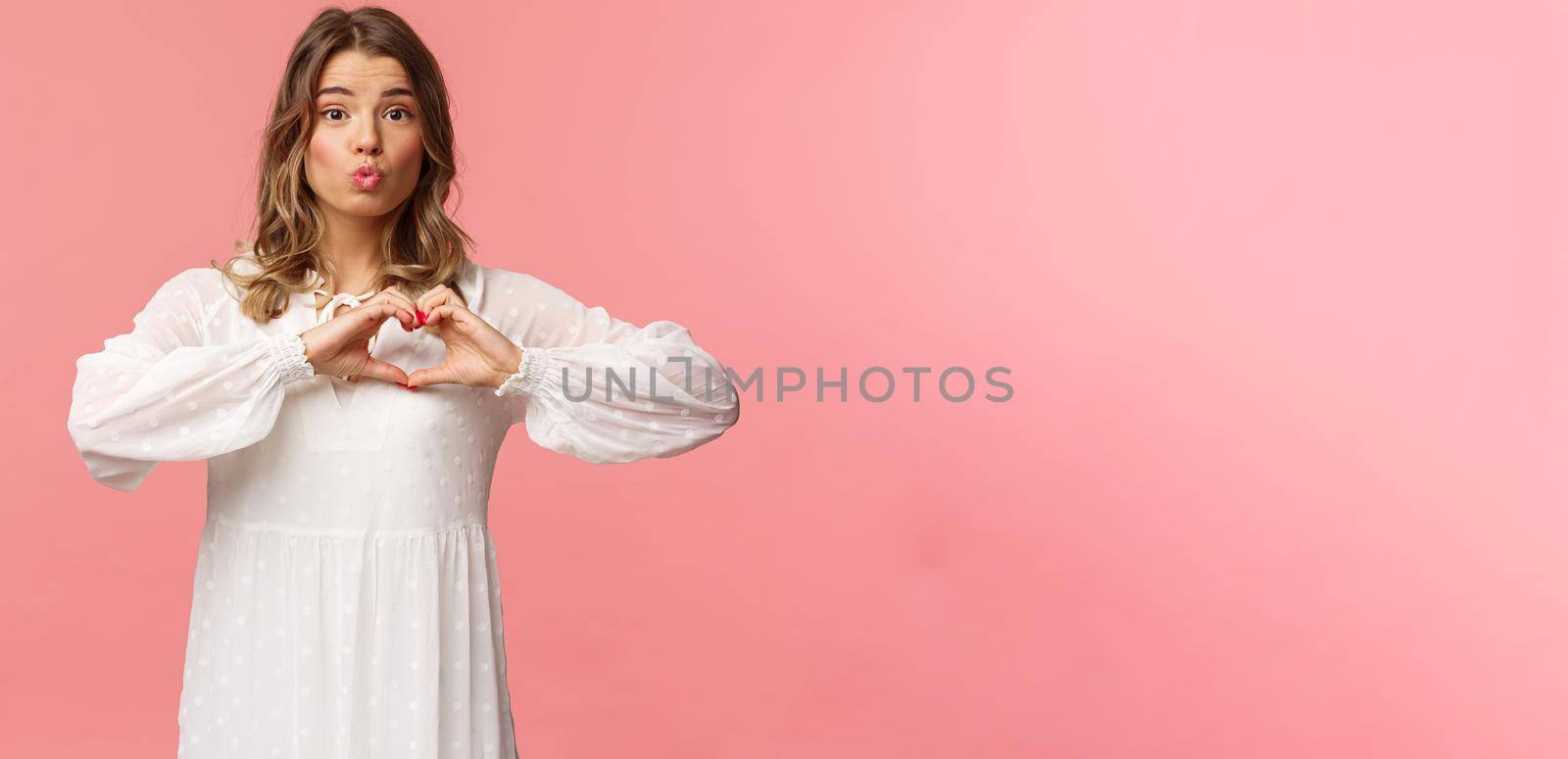 Beauty, fashion and women concept. Portrait of tender lovely young blond girl in beautiful white dress, fold lips in kiss and make heart sign near chest, standing pink background, show sympathy by Benzoix