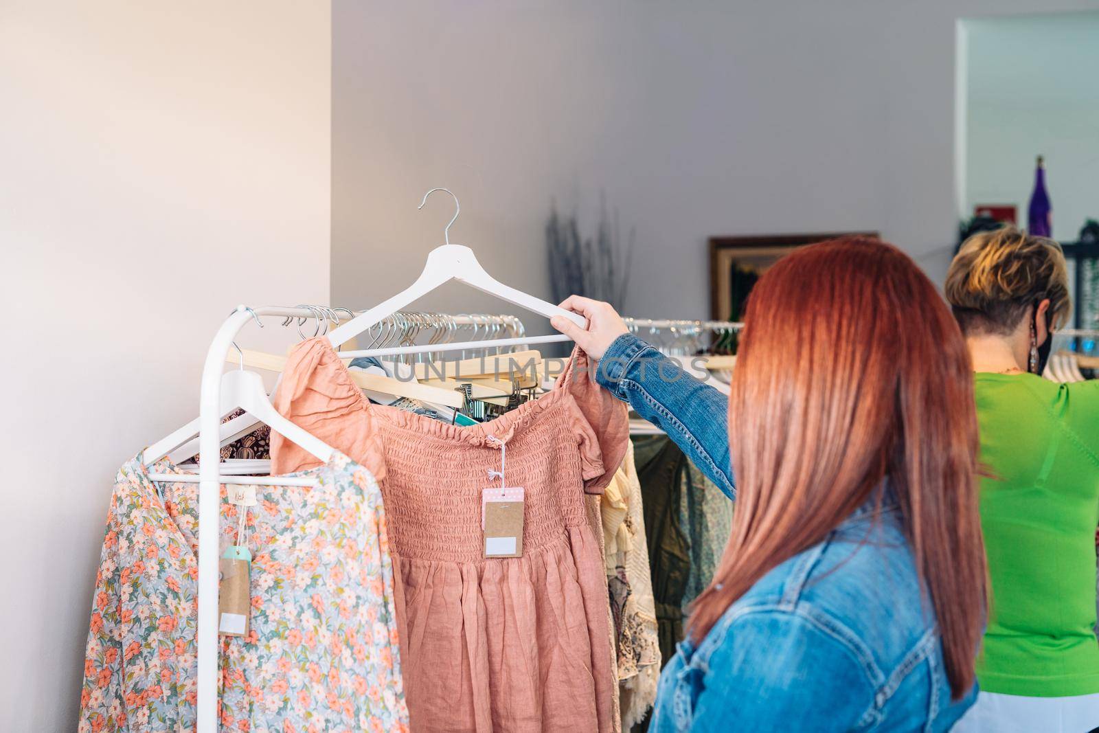 young red-haired woman buying clothes from a rack, in a small fashion shop. shopping concept. by CatPhotography