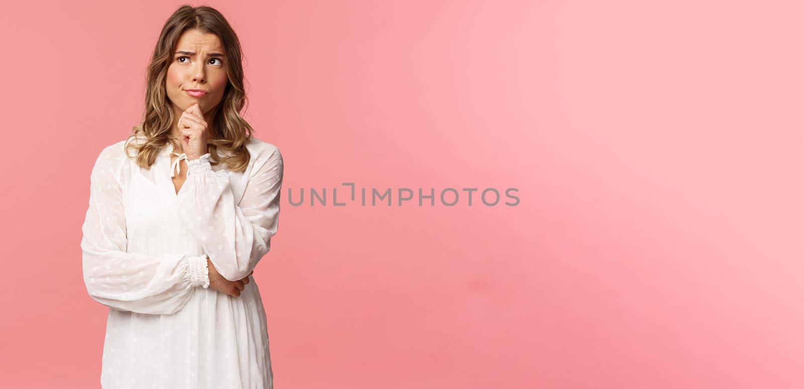 Beauty, fashion and women concept. Portrait of uncertain, serious-looking feminine young blond woman in white dress, touch chin, smirk and frowning thoughtful, look away thinking by Benzoix