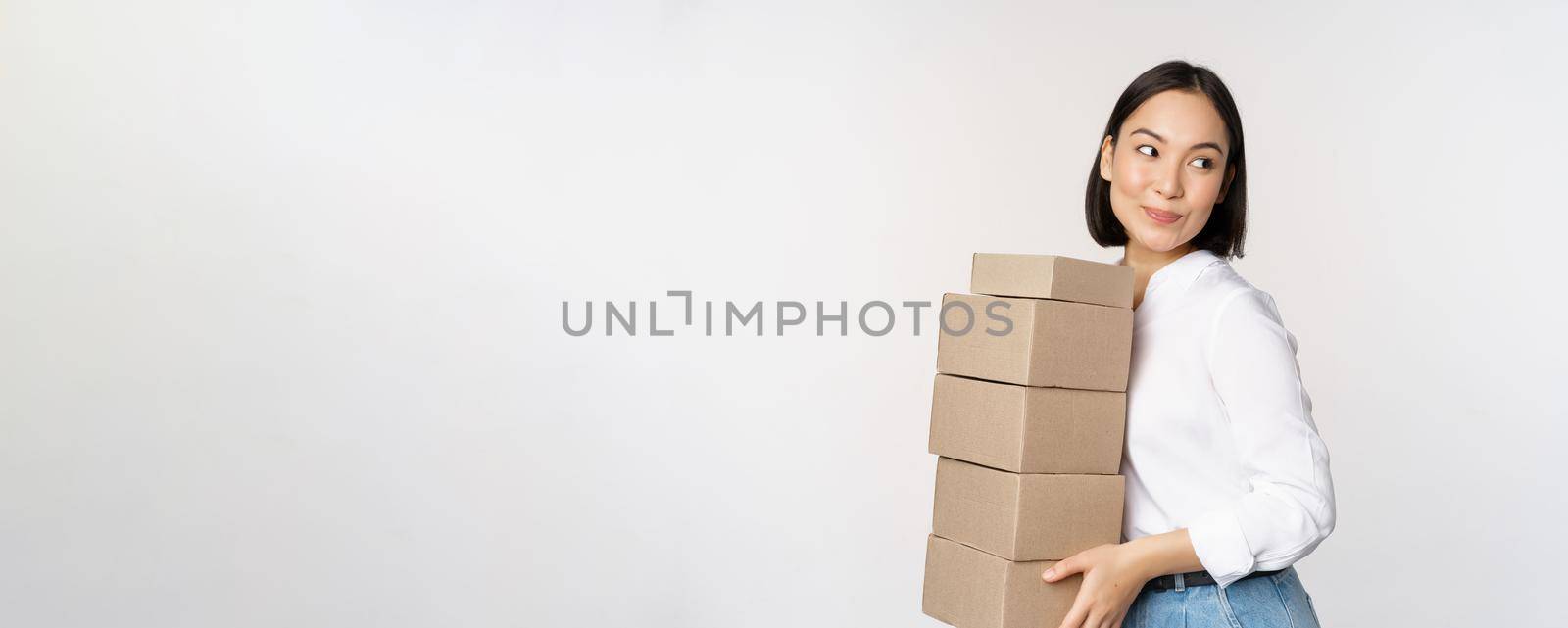 Portrait of young asian woman holding boxes, carry delivery goods. Korean female entrepreneur assemble order, standing voer white background.