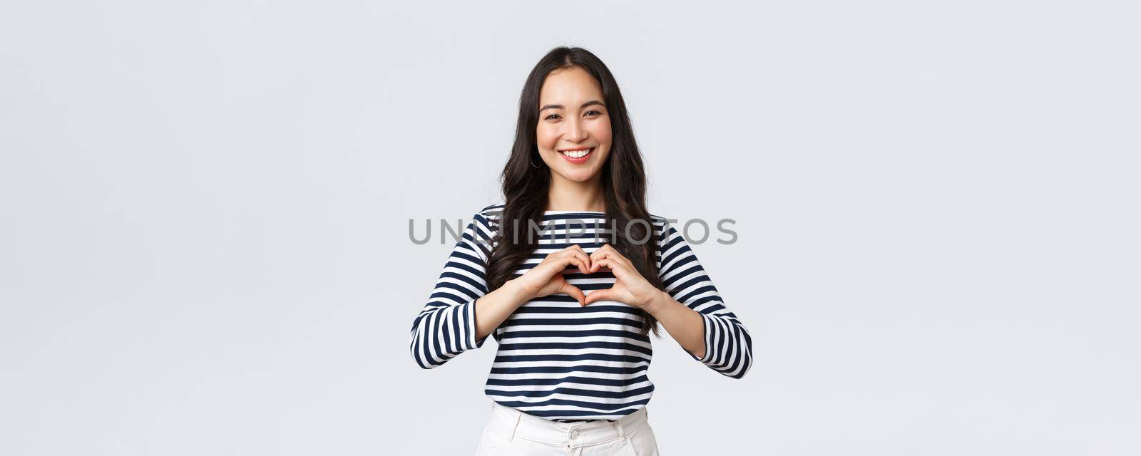 Lifestyle, people emotions and casual concept. Lovely smiling adorable asian woman showing heart sign and smiling, express sympathy or care, standing white background by Benzoix