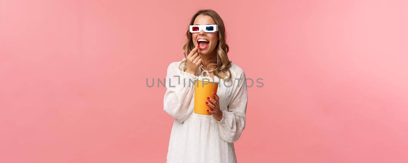 Leisure, going-out and spring concept. Portrait of attractive young woman in white dress enjoying watching interesting movie on full screen at cinema, eating popcorn and wearing 3d glasses.