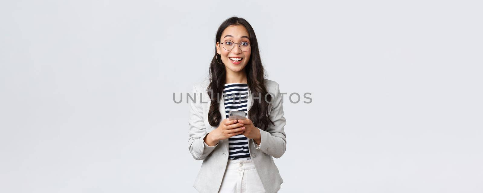 Business, finance and employment, female successful entrepreneurs concept. Cheerful happy asian businesswoman, office manager looking upbeat camera with smile, using smartphone.