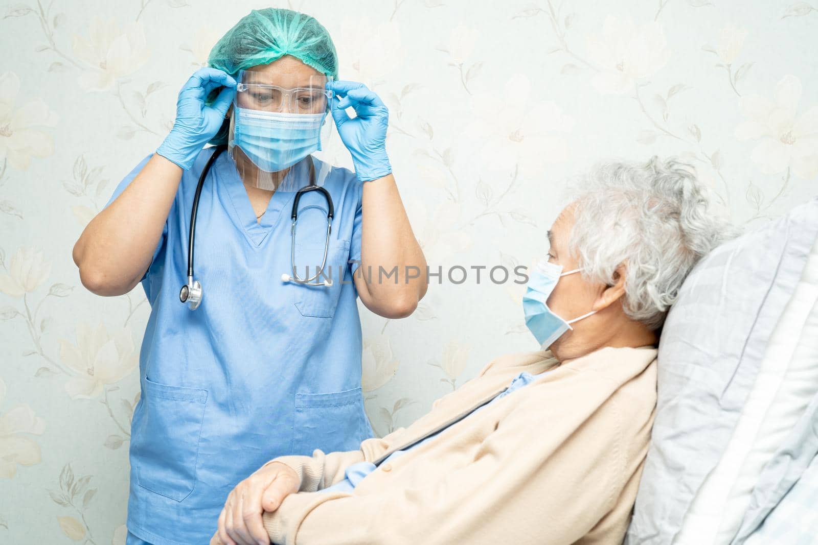 Asian doctor wearing face shield and PPE suit new normal to check patient protect safety infection Covid-19 Coronavirus outbreak at quarantine nursing hospital ward.