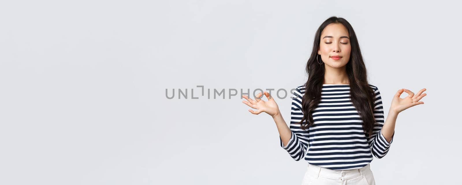 Lifestyle, people emotions and casual concept. Relaxed and patient smiling young asian woman with closed eyes meditating to calm down, do breathing exercises with hands in zen gesture.