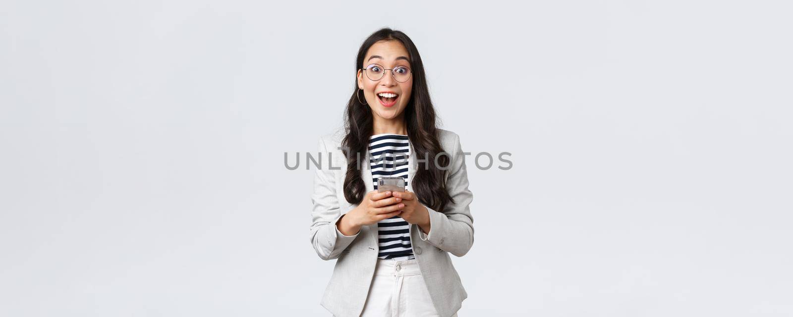 Business, finance and employment, female successful entrepreneurs concept. Cheerful happy asian businesswoman, office manager looking upbeat camera with smile, using smartphone by Benzoix