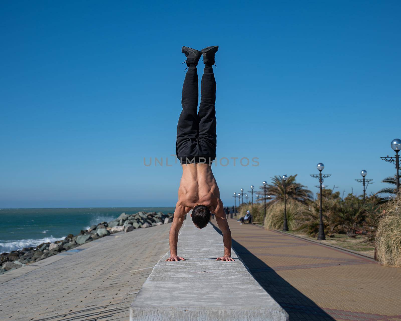 Shirtless man doing a handstand on the seashore. by mrwed54