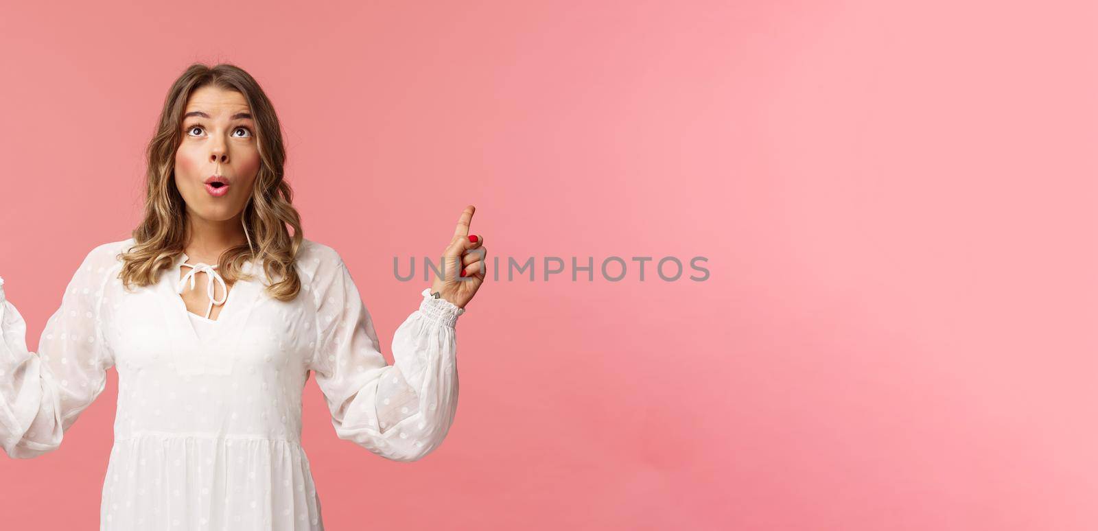 Excited beautiful caucasian blond woman in white dress, fold lips in excitement, looking pointing fingers up at something stunning and breathtaking, enjoying view, pink background by Benzoix