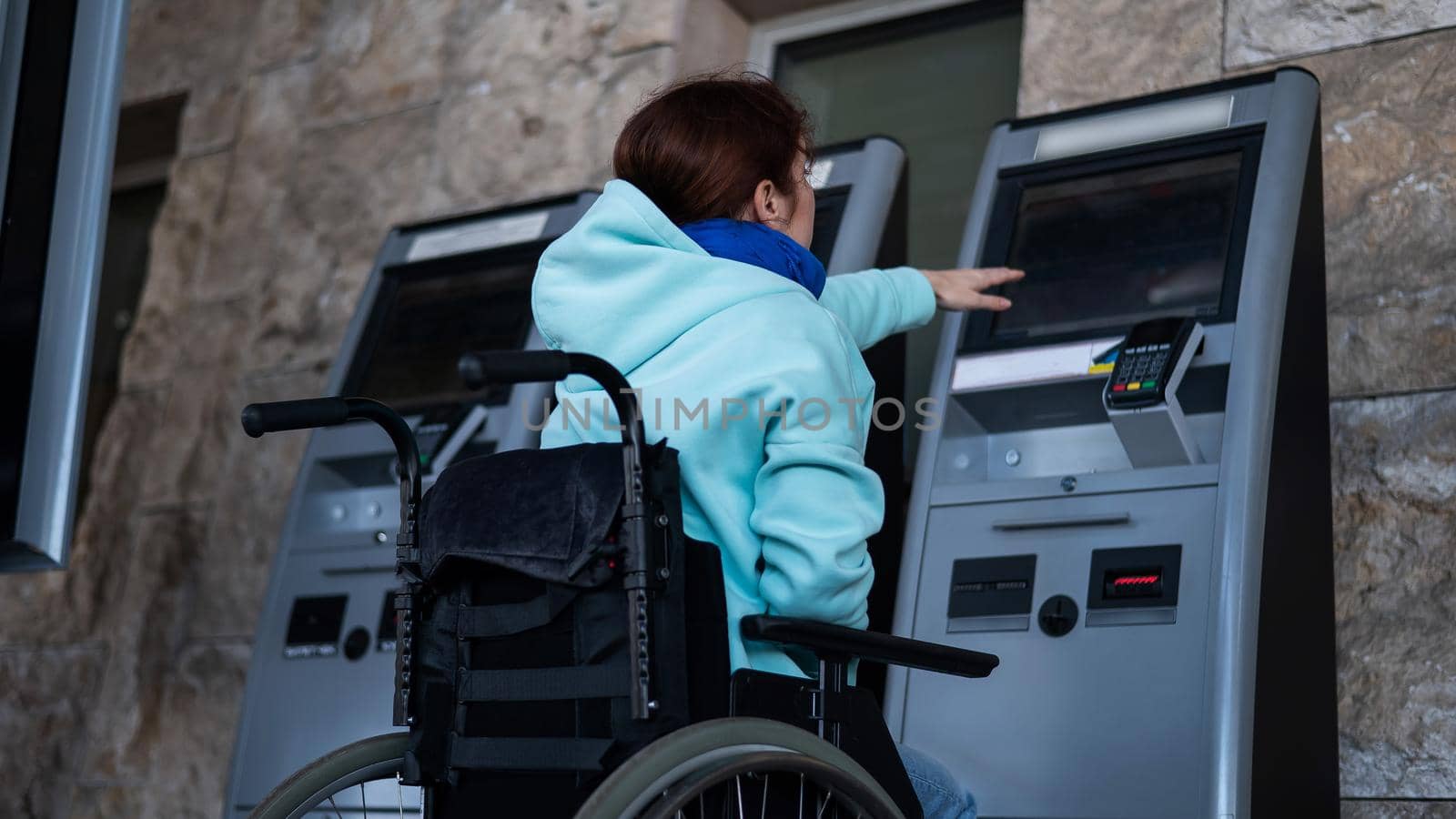 A Caucasian woman in a wheelchair does not reach the self-service checkout at the railway station. Hard-to-reach environment