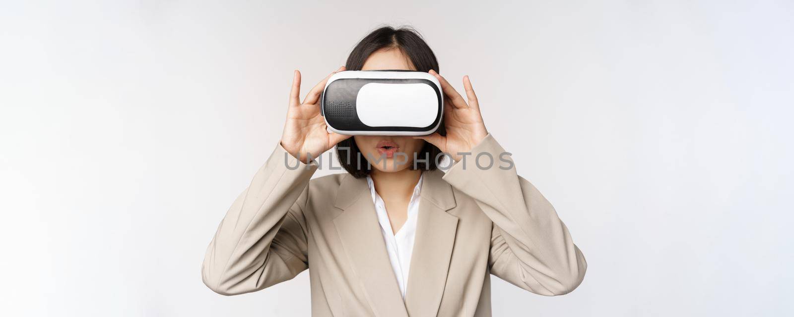 Amazed office woman, asian business person in suit, wearing vr headset, looking at smth in virtual reality glasses with impressed, wow face, white background by Benzoix