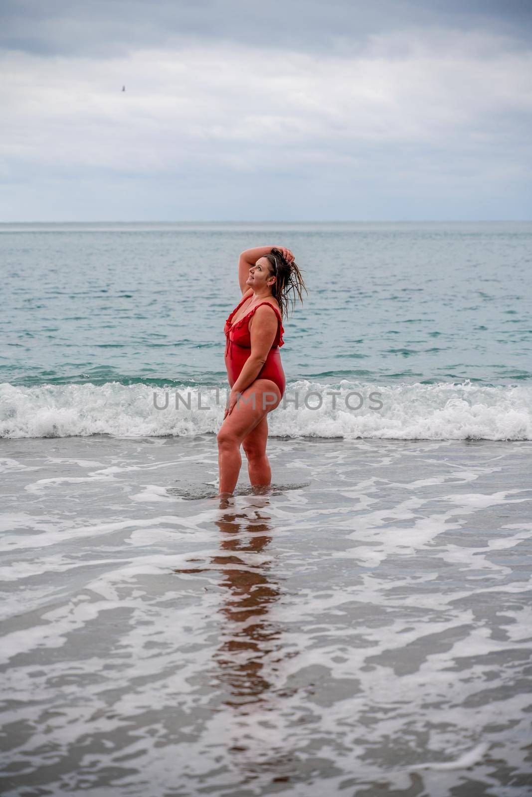 Woman in a bathing suit at the sea. A fat young woman in a red swimsuit enters the water during the surf.