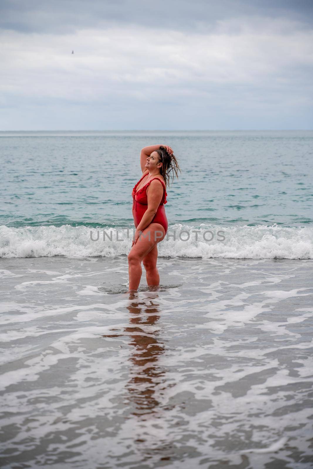 Woman in a bathing suit at the sea. A fat young woman in a red swimsuit enters the water during the surf by Matiunina