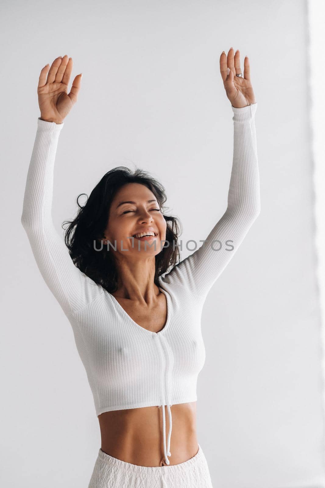 a female yogi in white clothes with her hands up meditates in the Yoga hall. by Lobachad