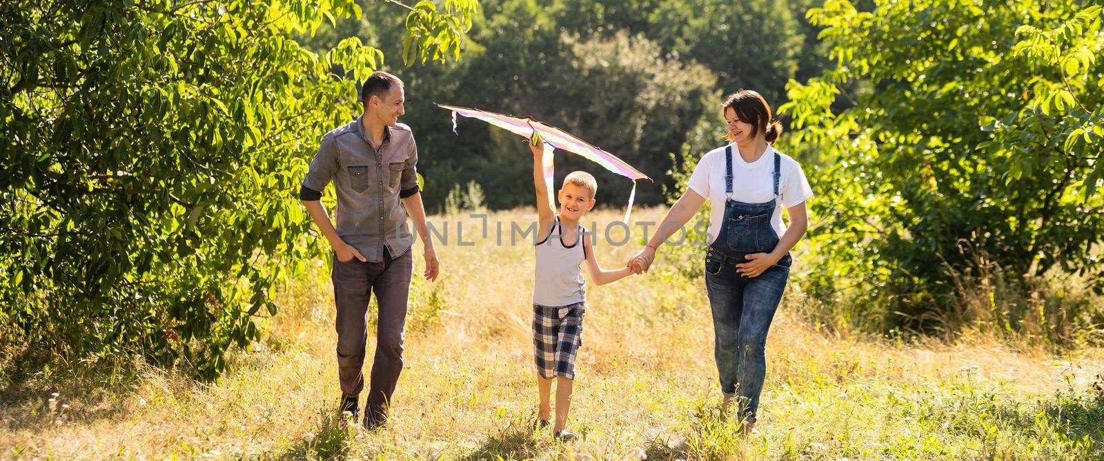 Happy family with pregnant wife fly a kite together in summer field