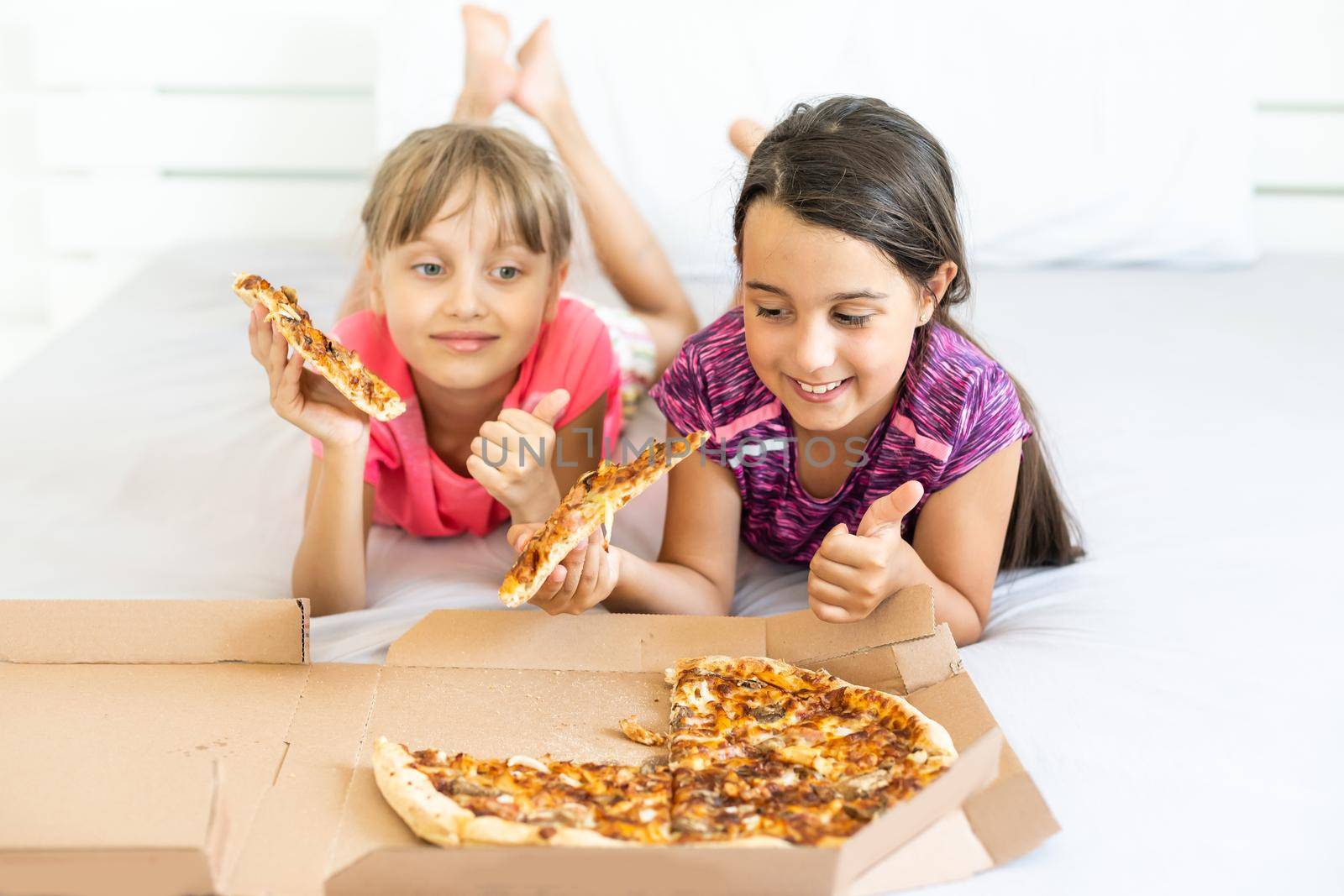 Two little girls eating pizza at home by Andelov13