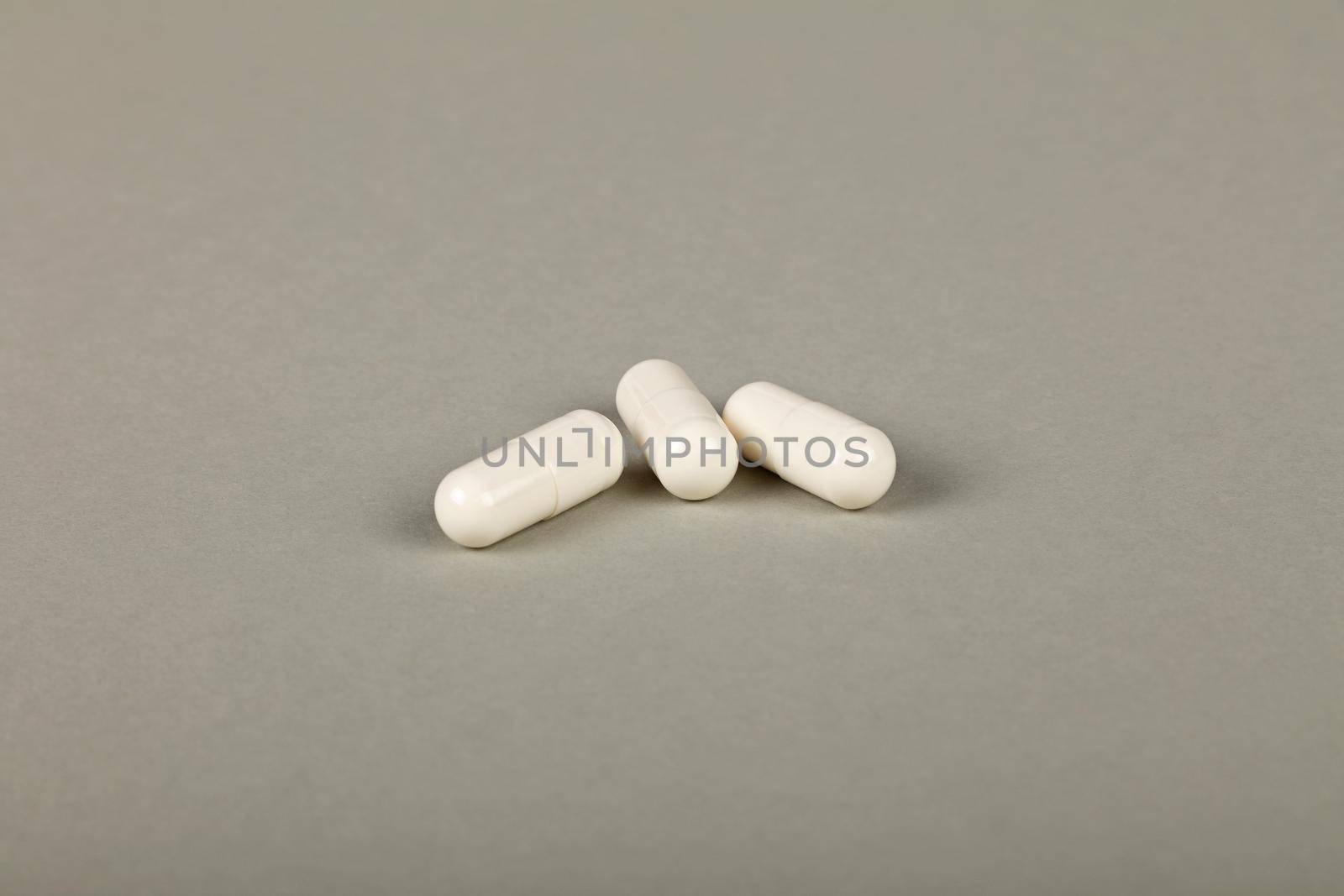 Close up three white gel cap pills of medicine over grey background with copy space, high angle view