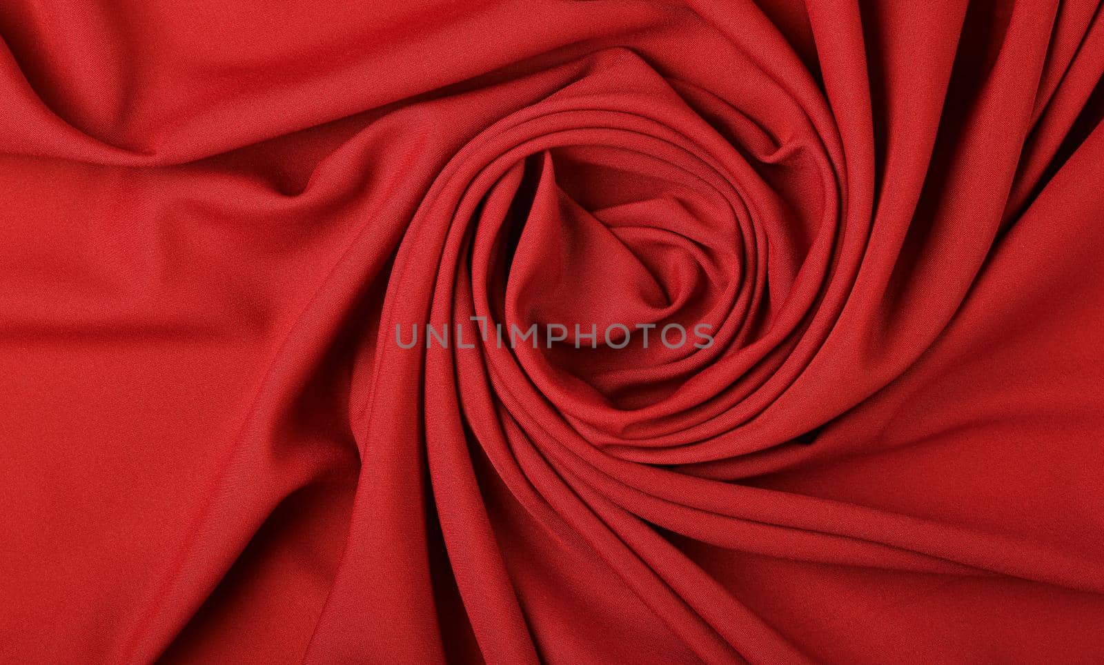 Close up abstract textile background of spiral shaped red folded pleats of fabric, elevated top view, directly above