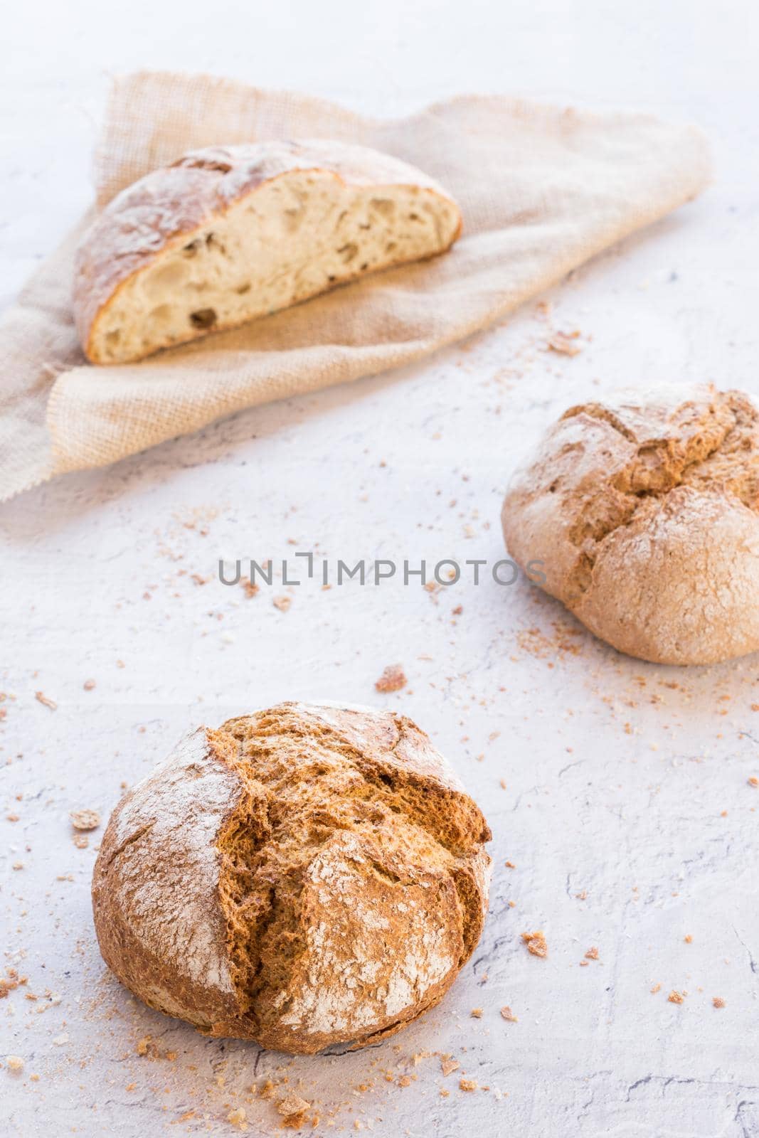 image at forty-five degrees vertically of three ecological rustic breads distributed in the shape of a triangle on a white surface and a beige cloth surrounded by crumbs with natural light