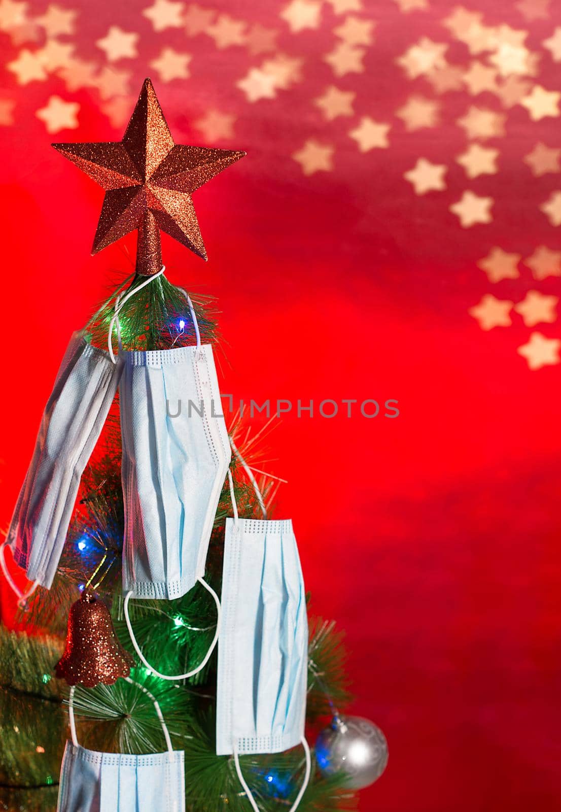 2020 Christmas tree decorated with colored lights ornaments and surgical masks with a red star at the tip and a red background with bokeh of stars