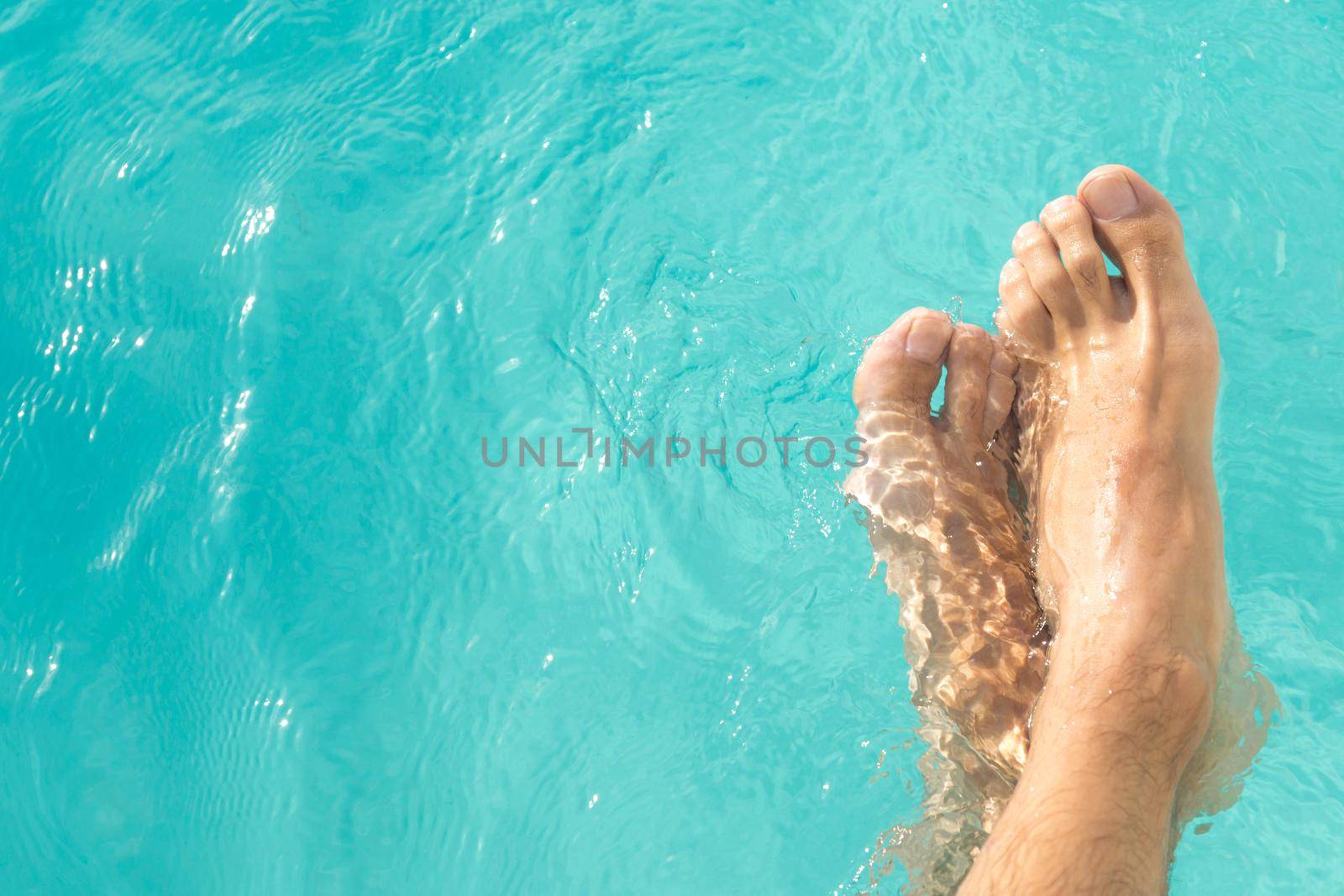 pretty man's feet in the turquoise blue pool water horizontal background