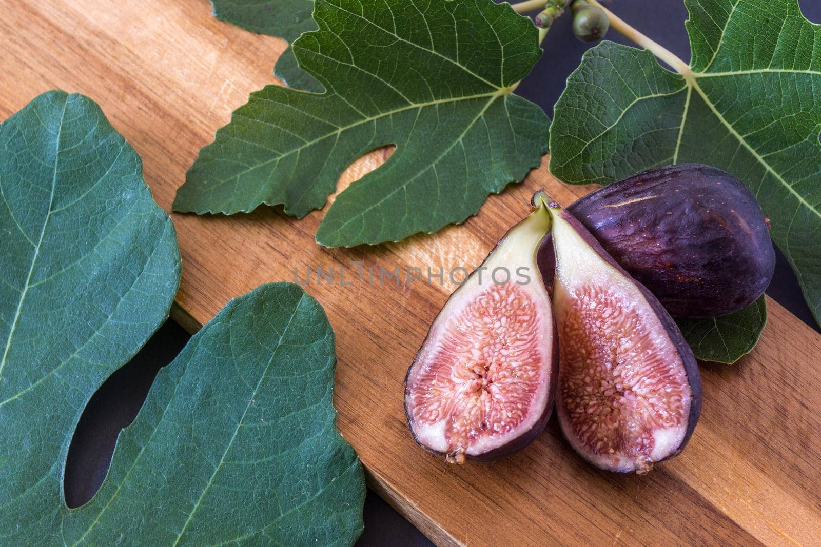 fresh cut figs on a brown wooden board surrounded by fig leaves in landscape format with natural lighting