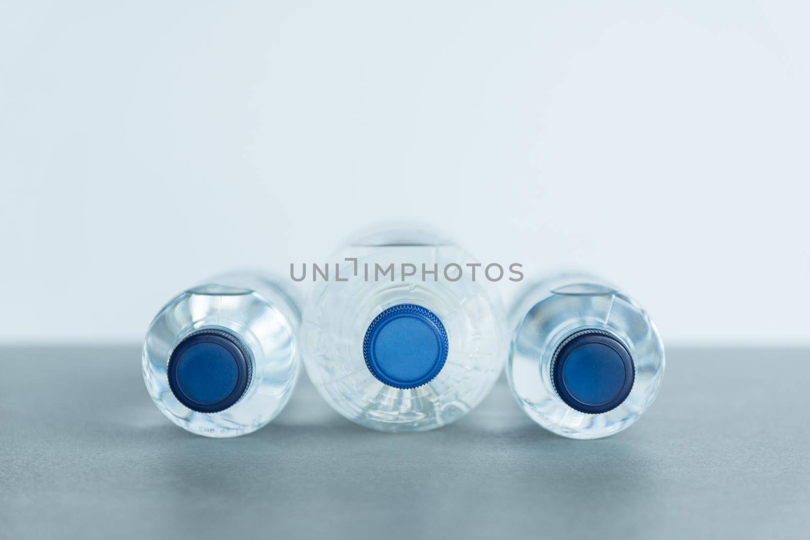 three plastic bottles full of mineral water lying on the front view of the big one and the two of the smaller ones with blue caps on a white background