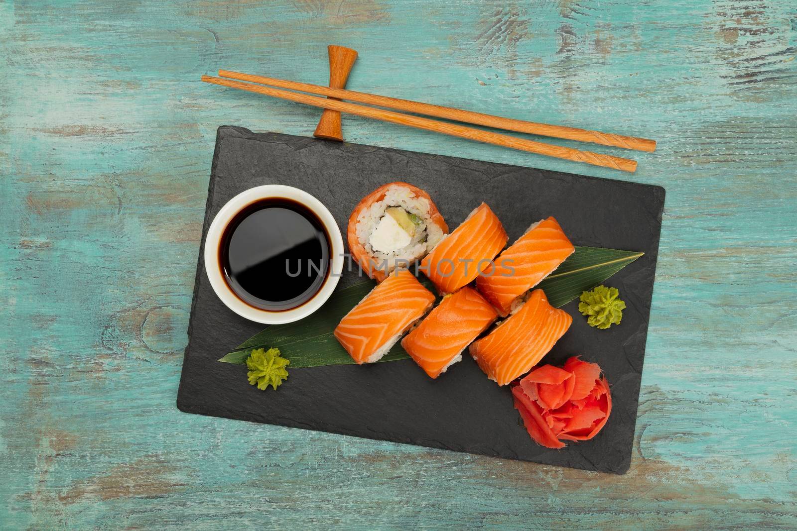 Close up set of six Philadelphia sushi rolls with raw salmon served on black slate board on blue table, elevated top view, directly above