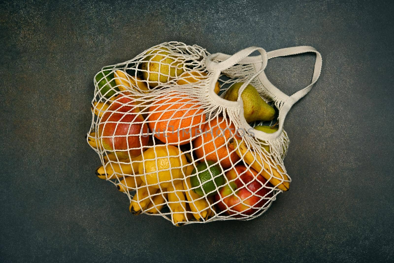 Close up assorted fresh fruits in reusable string mesh shopping bag on the floor or table, elevated top view, directly above