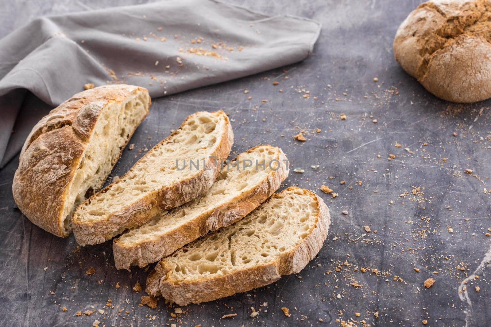 image at forty-five degrees of an organic bread divided into slices placed in a fan shape on a dark surface surrounded by crumbs and a gray cloth with natural light