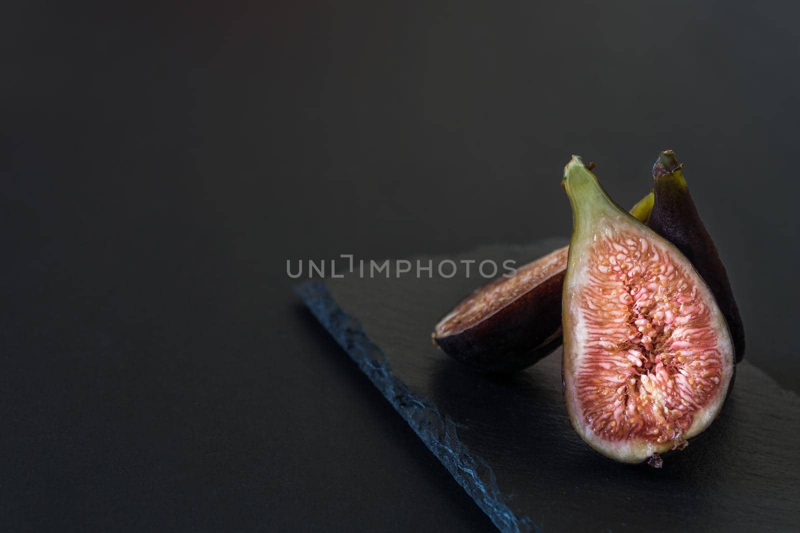 fresh sliced figs placed vertically on black slate table on black background horizontally with natural light