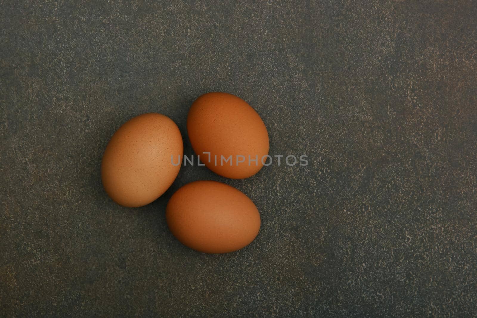 Close up three brown chicken eggs on dark grunge table surface, elevated top view, directly above