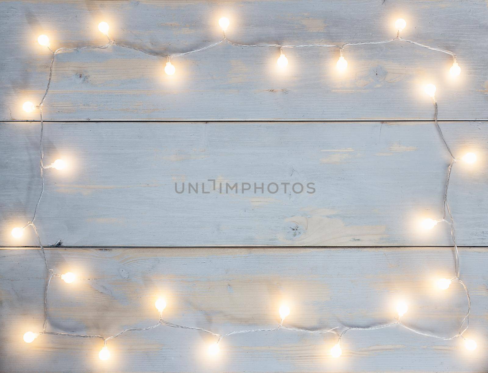 garland of round christmas lights with warm color placed in the form of a frame on light background of wooden planks