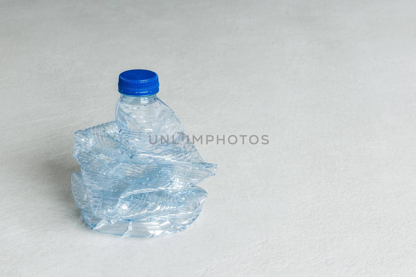 horizontal image of empty blue plastic bottle crushed for recycling on gray background