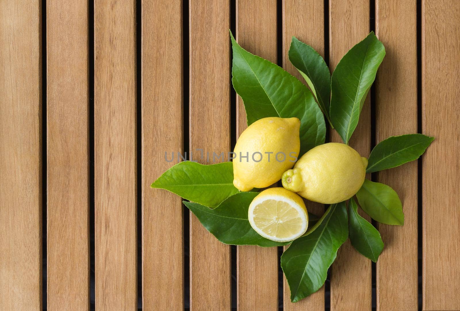 horizontal image from above of lemons on lemon leaves bed on vertical brown wooden slat table