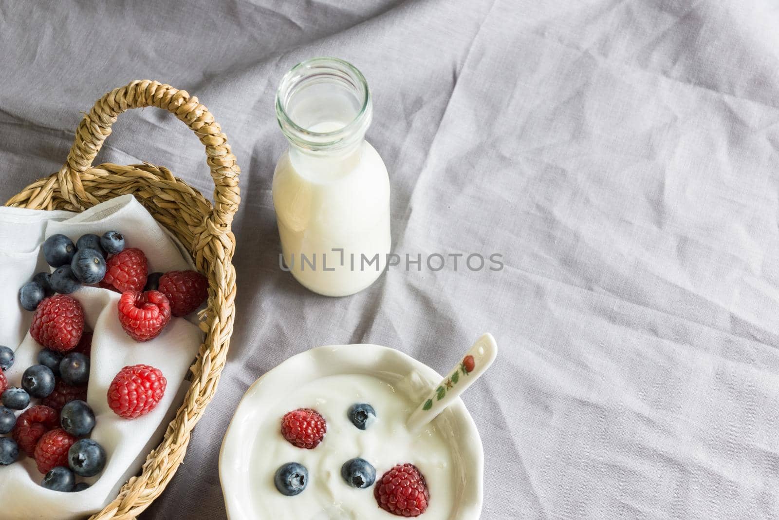 zenital shot to a bowl of natural yogurt with raspberries and blueberries with bottle of milk and fruit inside a wicker basket in landscape