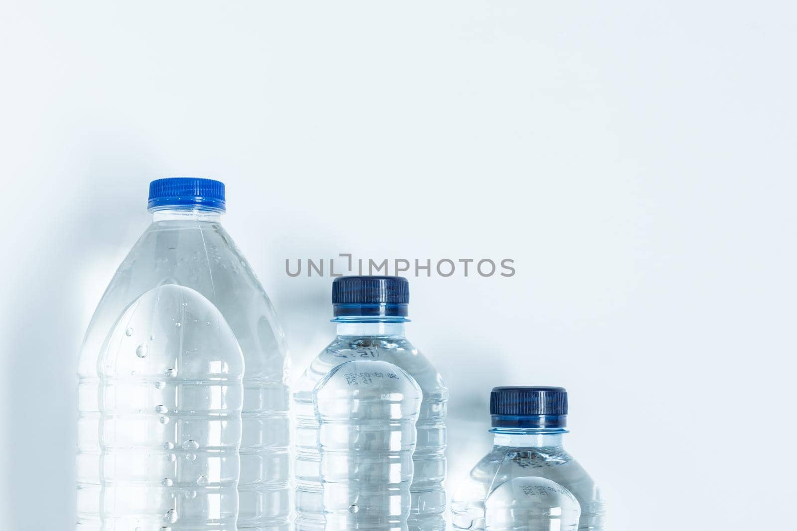 three plastic bottles with blue caps filled with mineral water placed on ladder viewed from above on white background