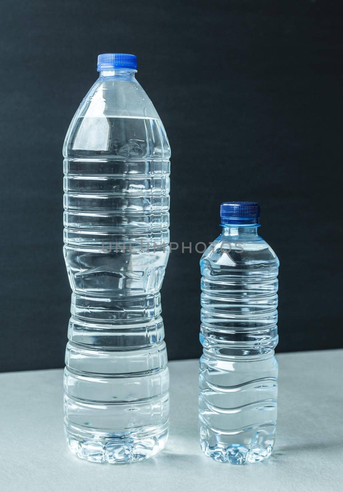 two plastic bottles filled with mineral water one large and one small with blue caps and black background